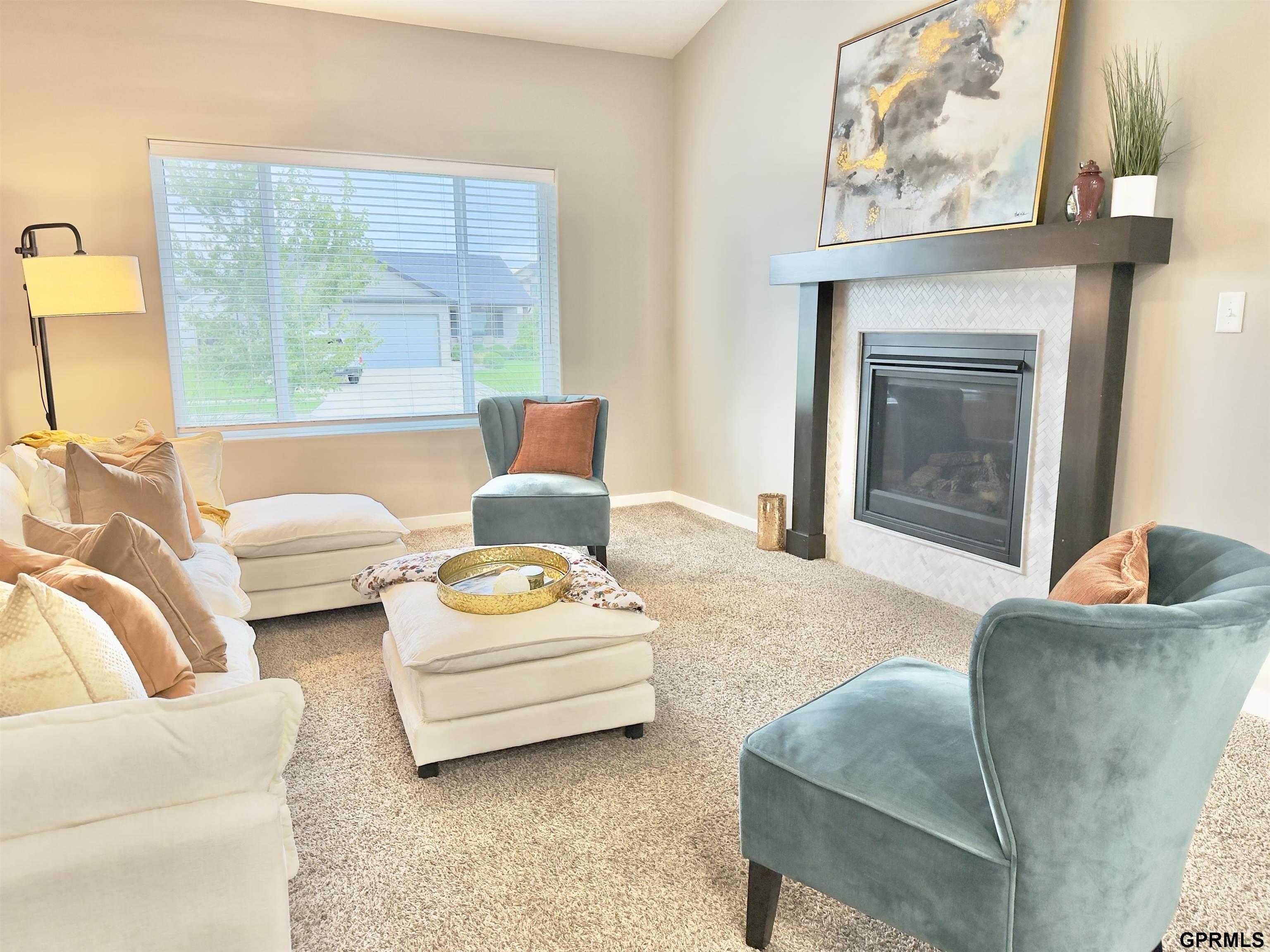 Furnished living room with a tiled fireplace, cream sofas, teal chairs, and a large window.