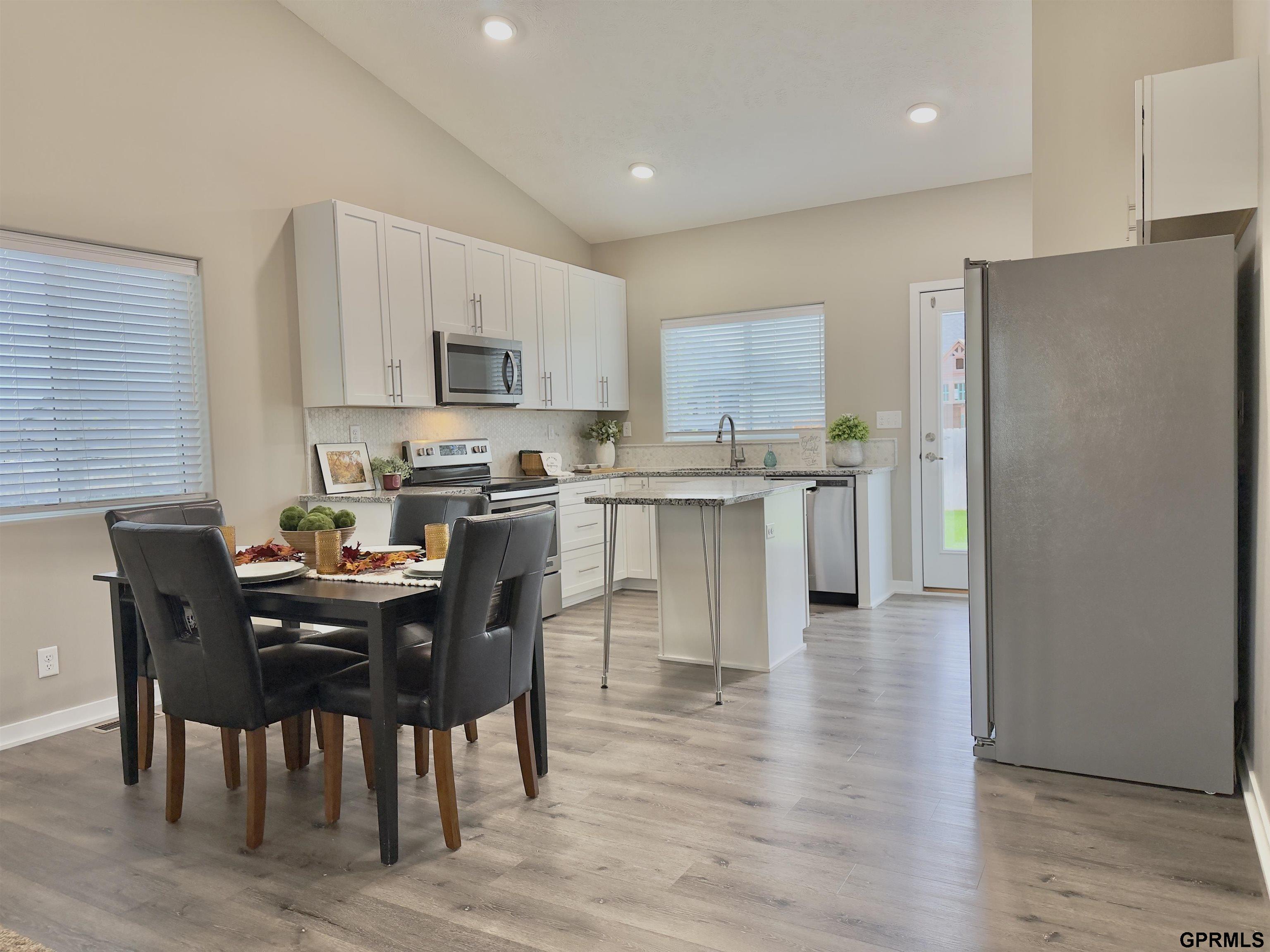 Kitchen and dining area with white cabinets, stainless appliances, a center island, and a dark dining set.