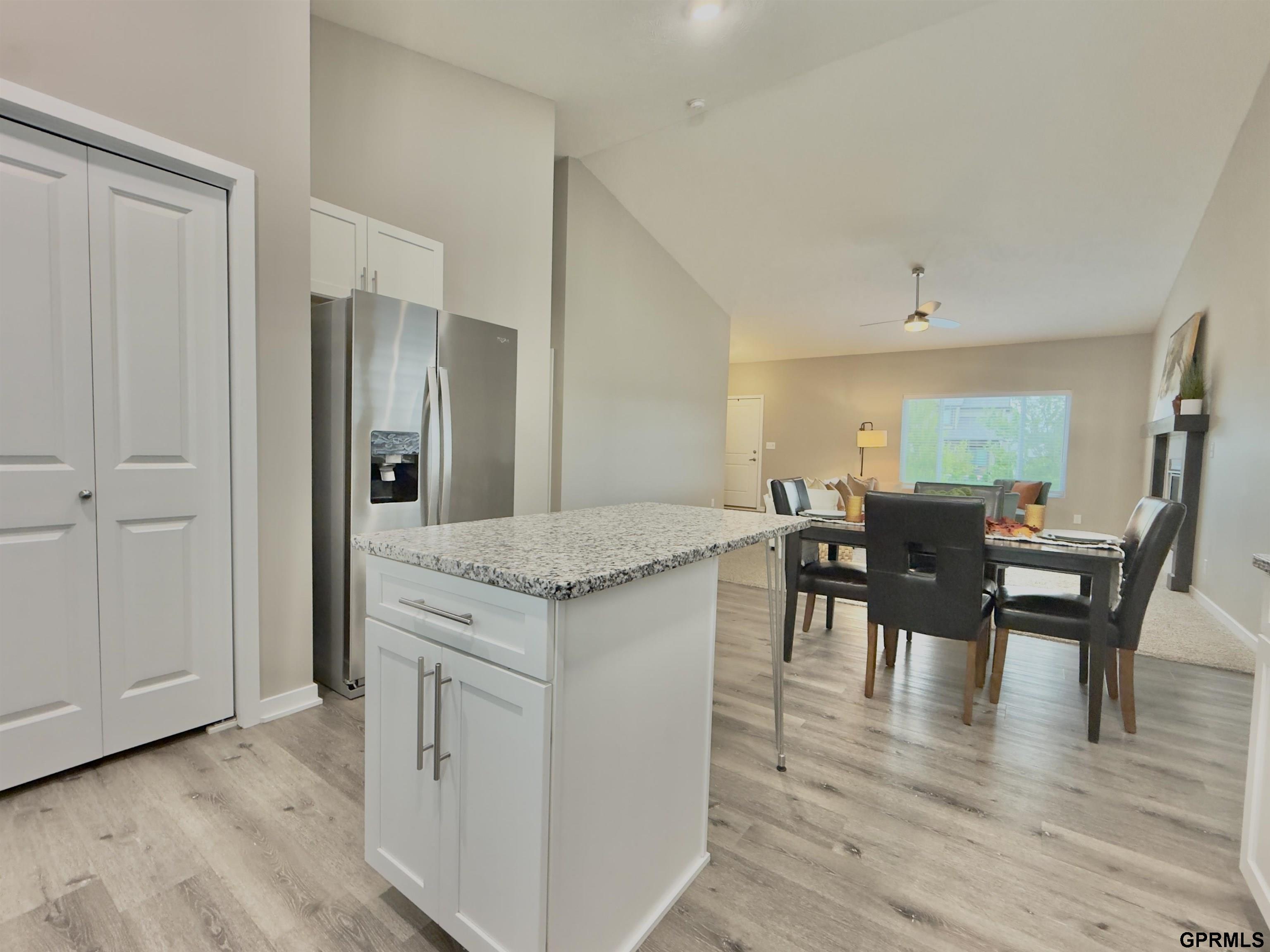 Open-plan kitchen with a granite island and stainless steel refrigerator beside a staged dining area.