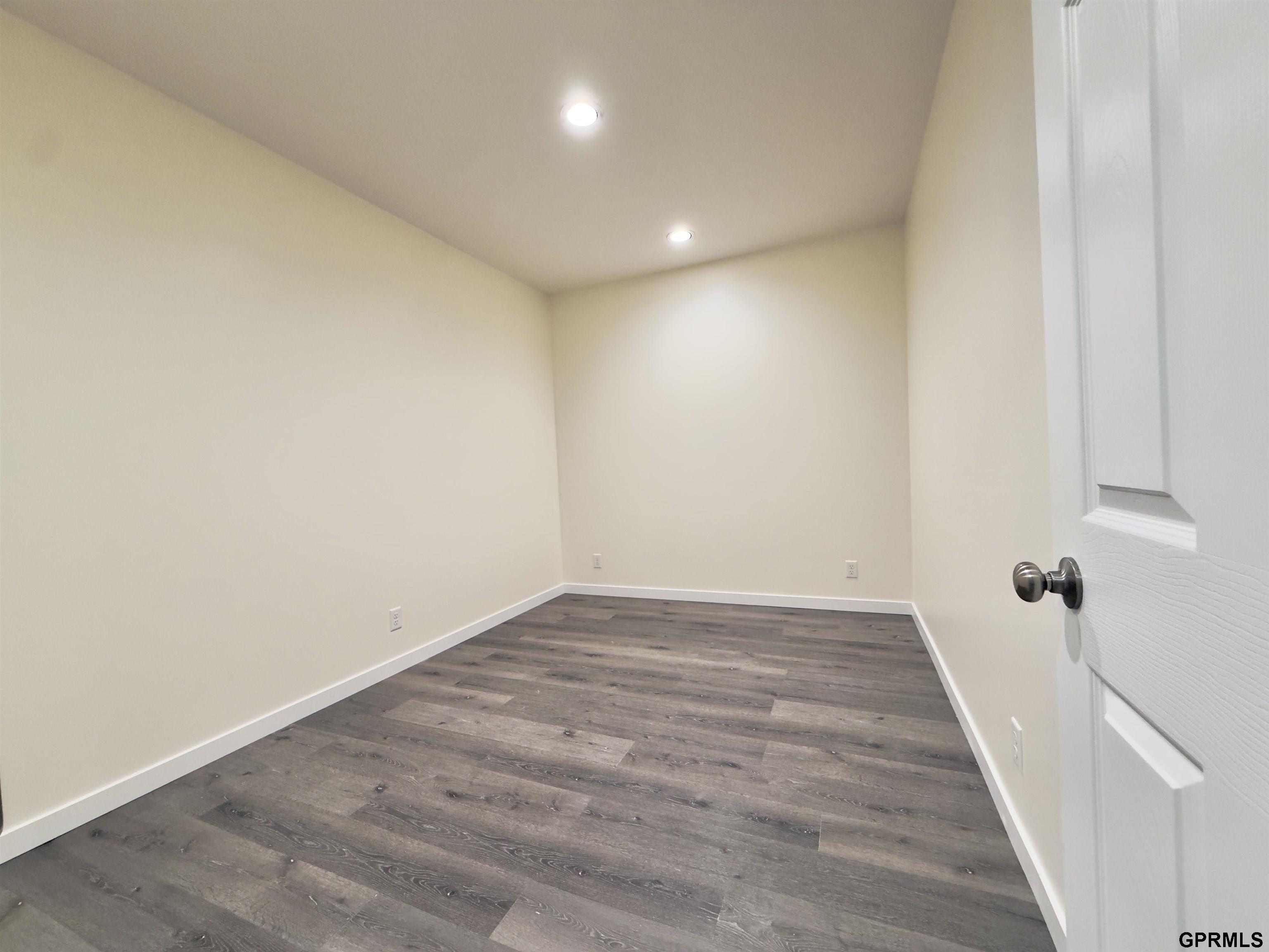 Empty room with dark plank flooring, recessed lights, and a white paneled door.