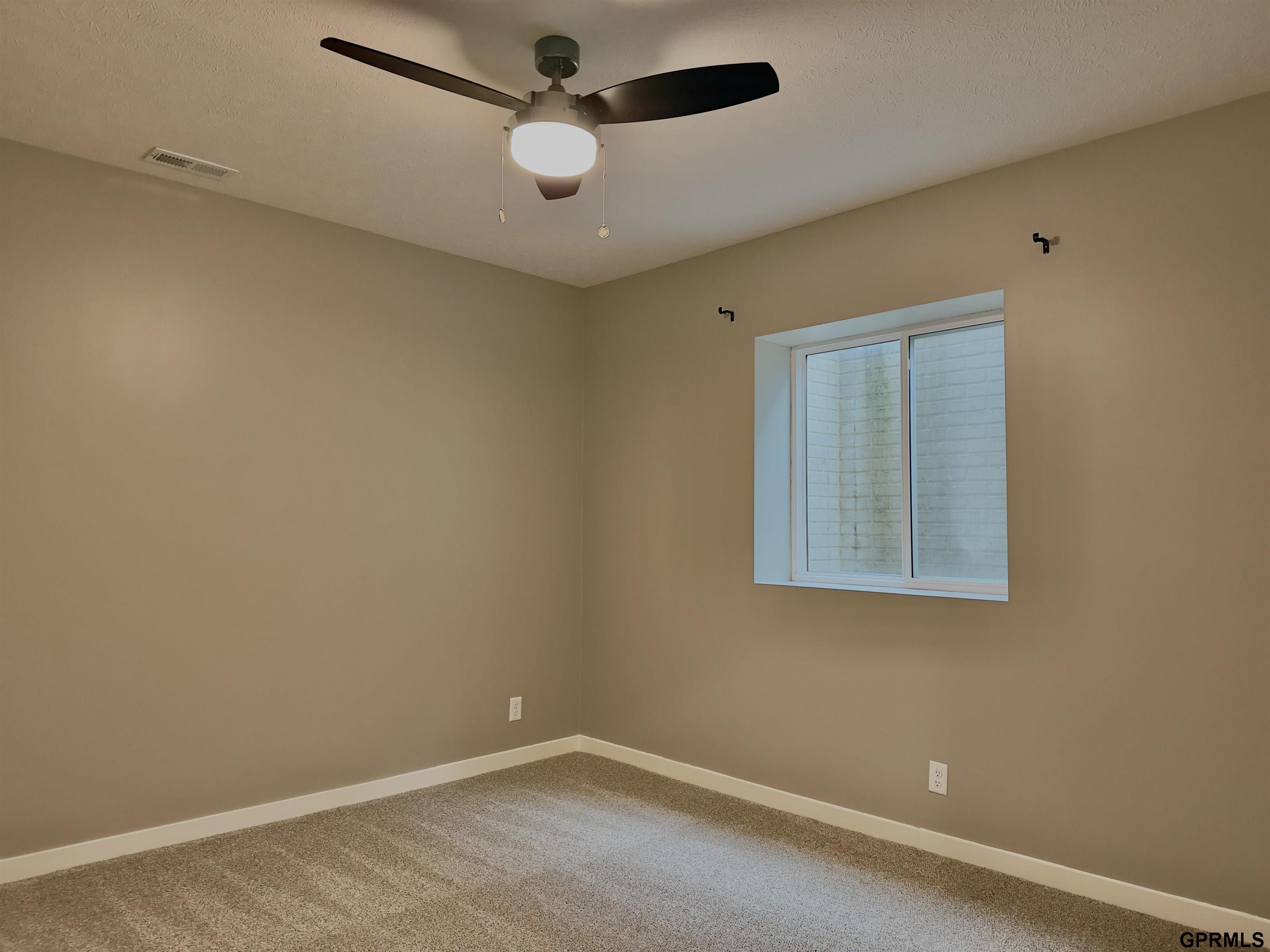 Empty carpeted room with beige walls, a ceiling fan, and a window.