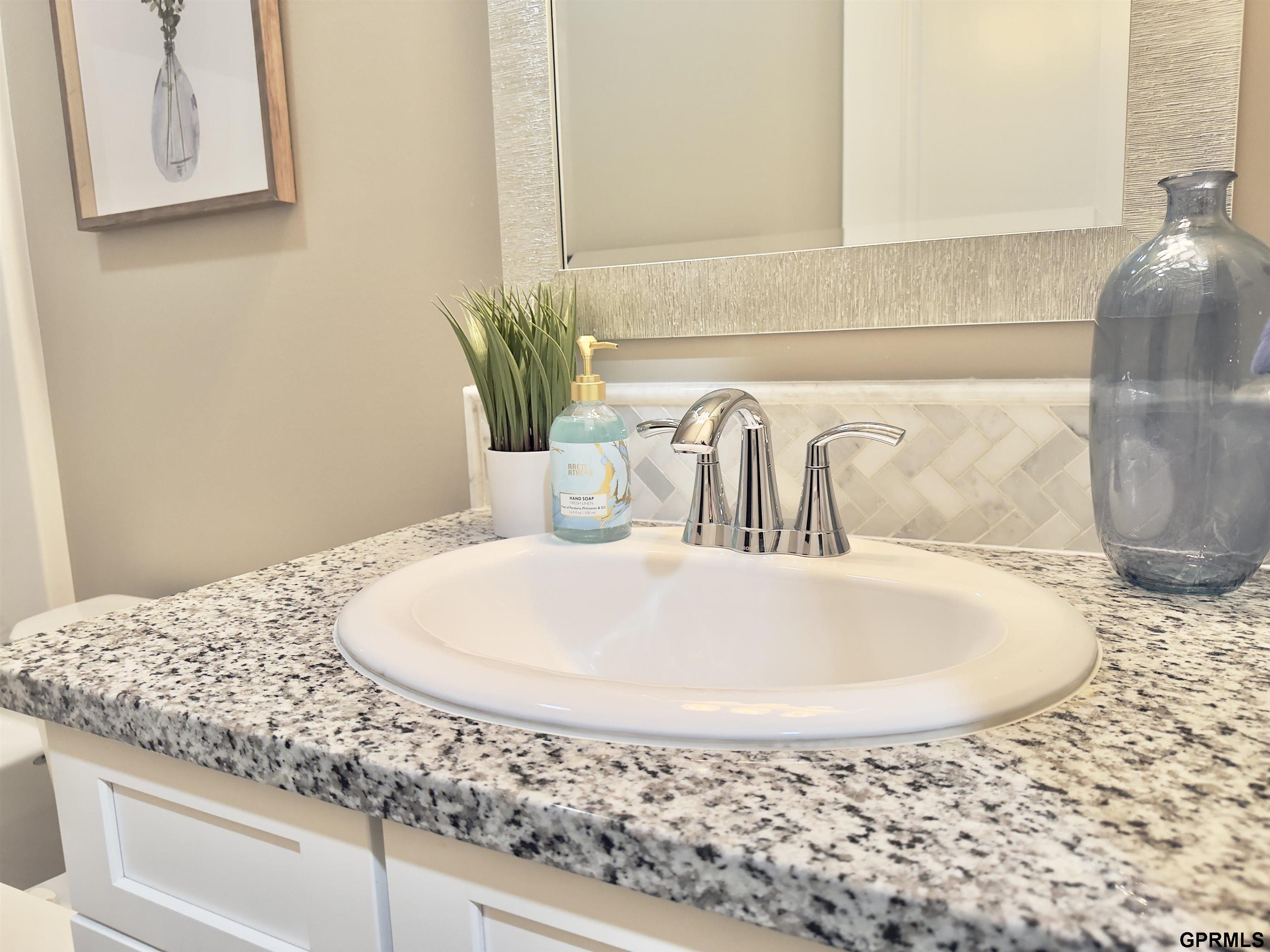Bathroom vanity with an oval sink, granite countertop, chrome faucet, and herringbone tile backsplash.