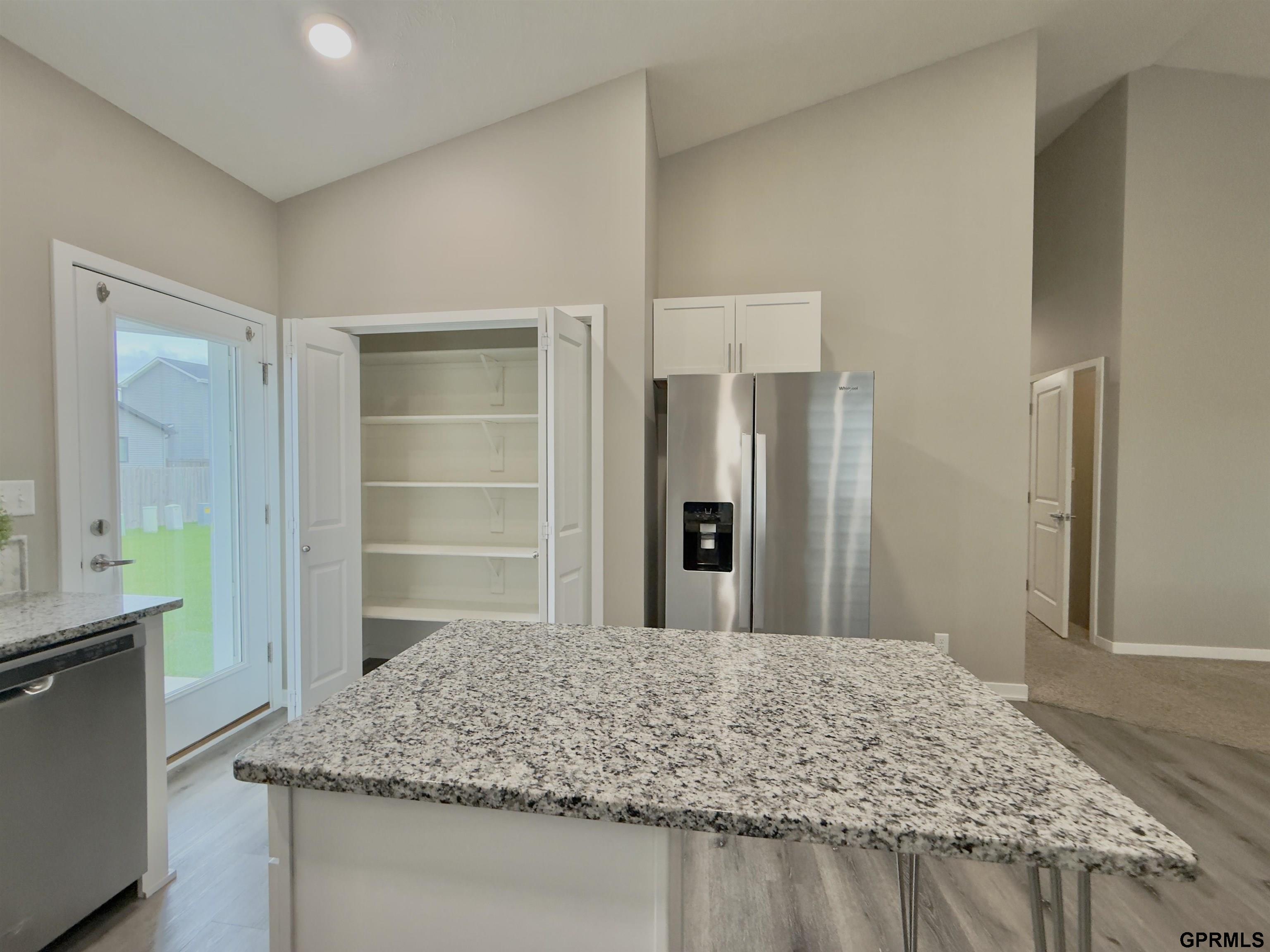 Kitchen with a large granite island, stainless steel refrigerator, and open pantry shelves.