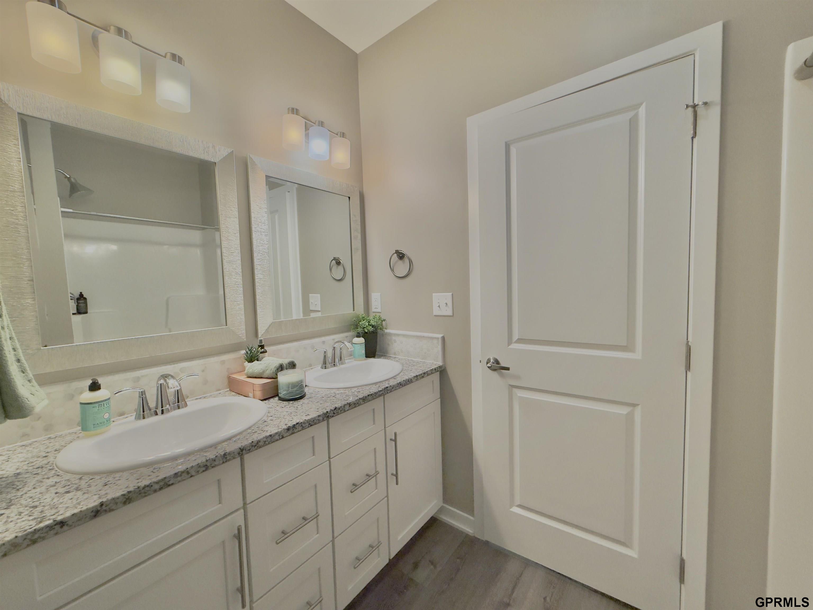Bathroom with a double-sink vanity, speckled countertop, large mirrors, and white cabinetry.