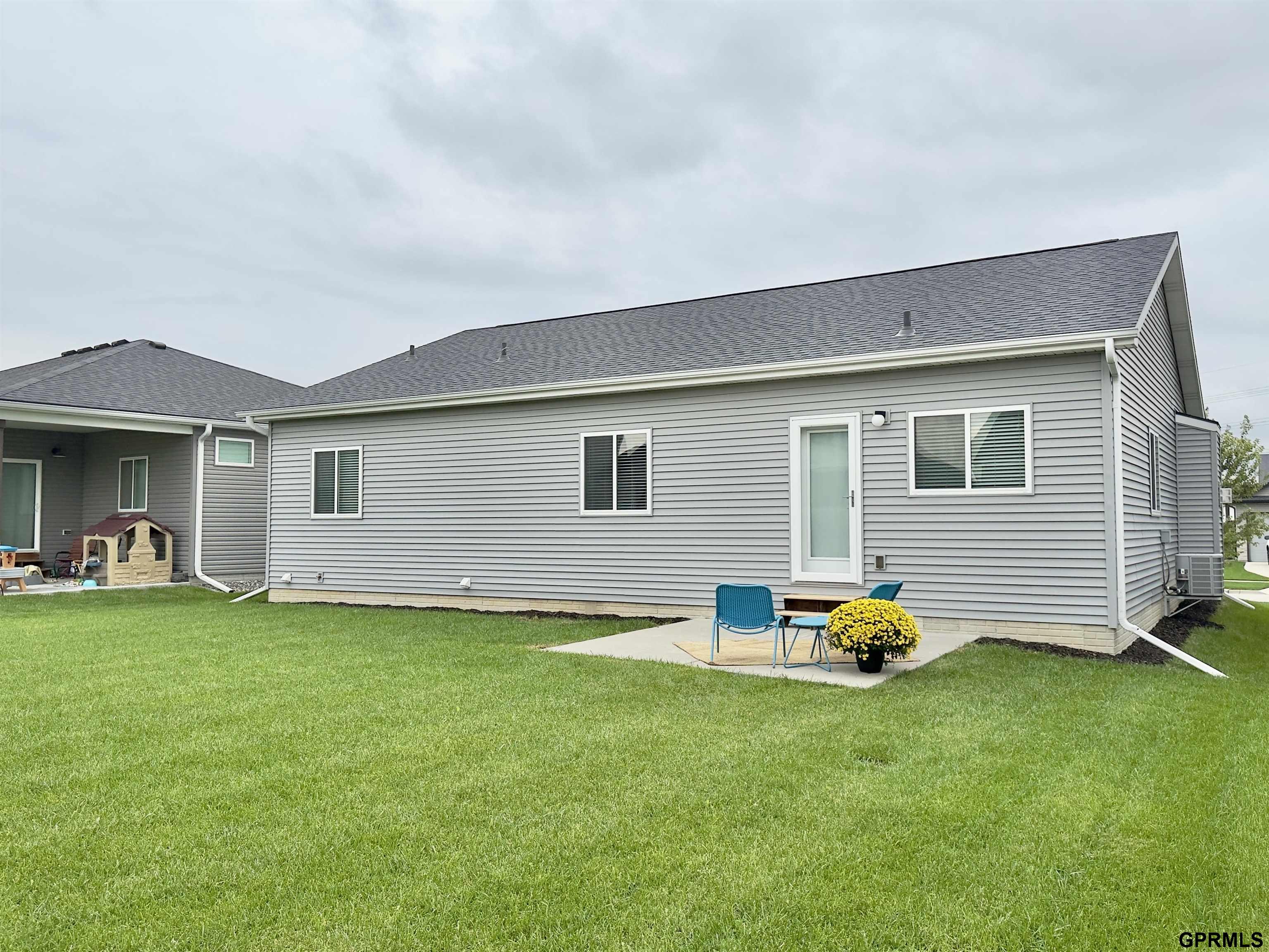 Gray-sided home’s rear exterior with a small patio, blue chairs, and a potted yellow flower.