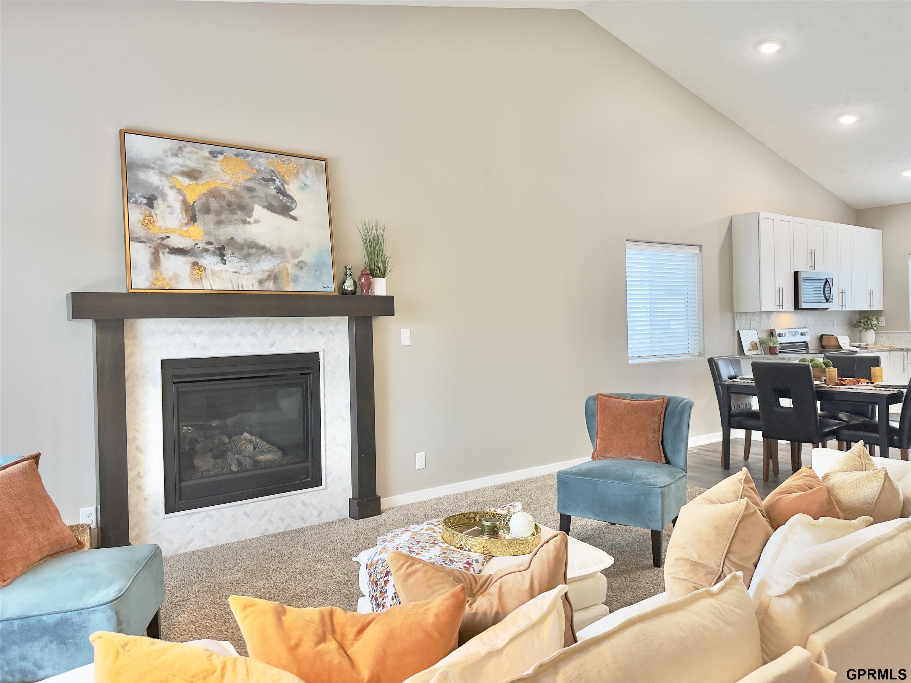 Living room with a white-tile fireplace, vaulted ceiling, blue chairs, and an adjoining dining area.