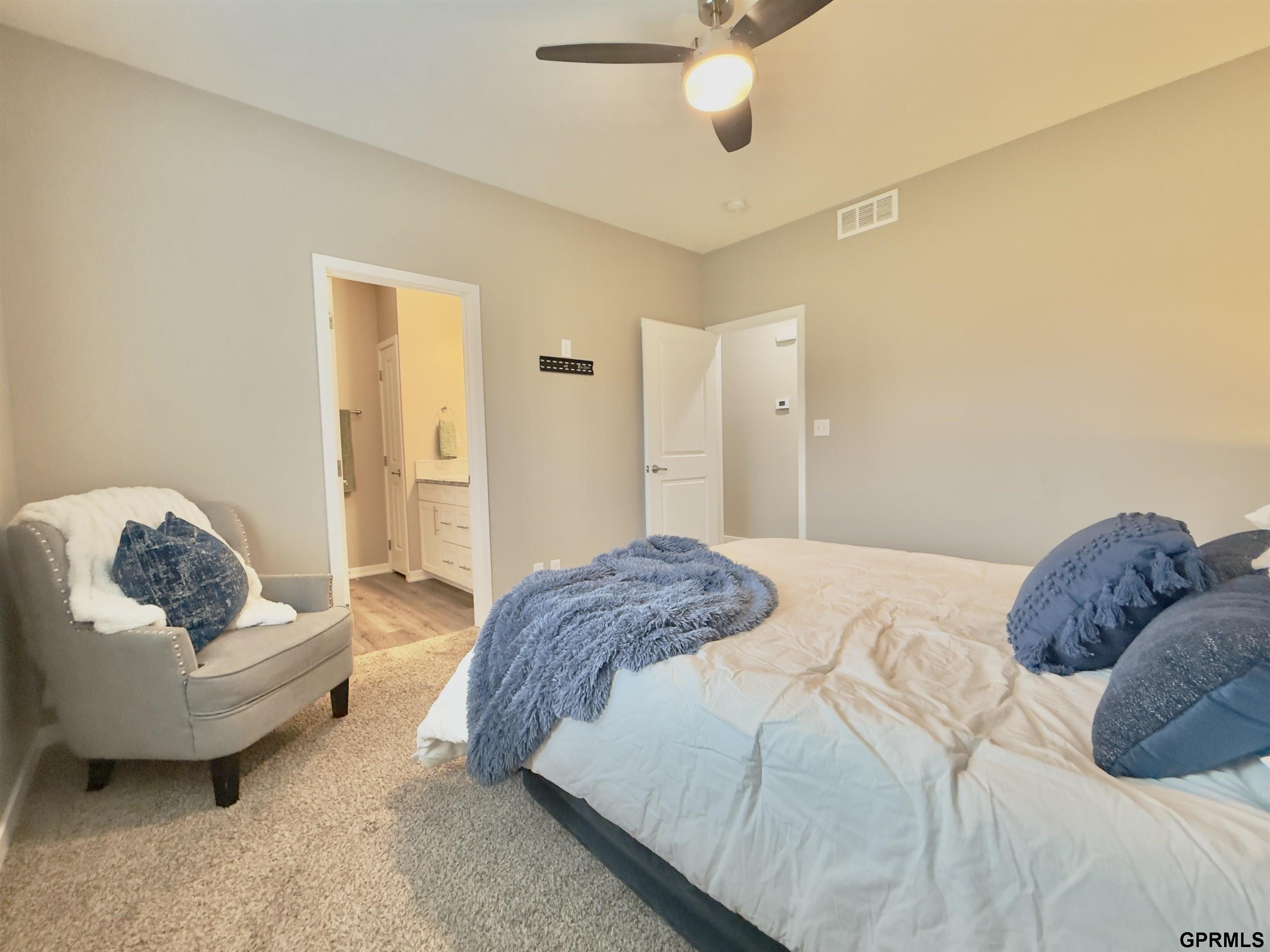 Furnished bedroom with blue and white bedding, a gray chair, and an open doorway to the bathroom.