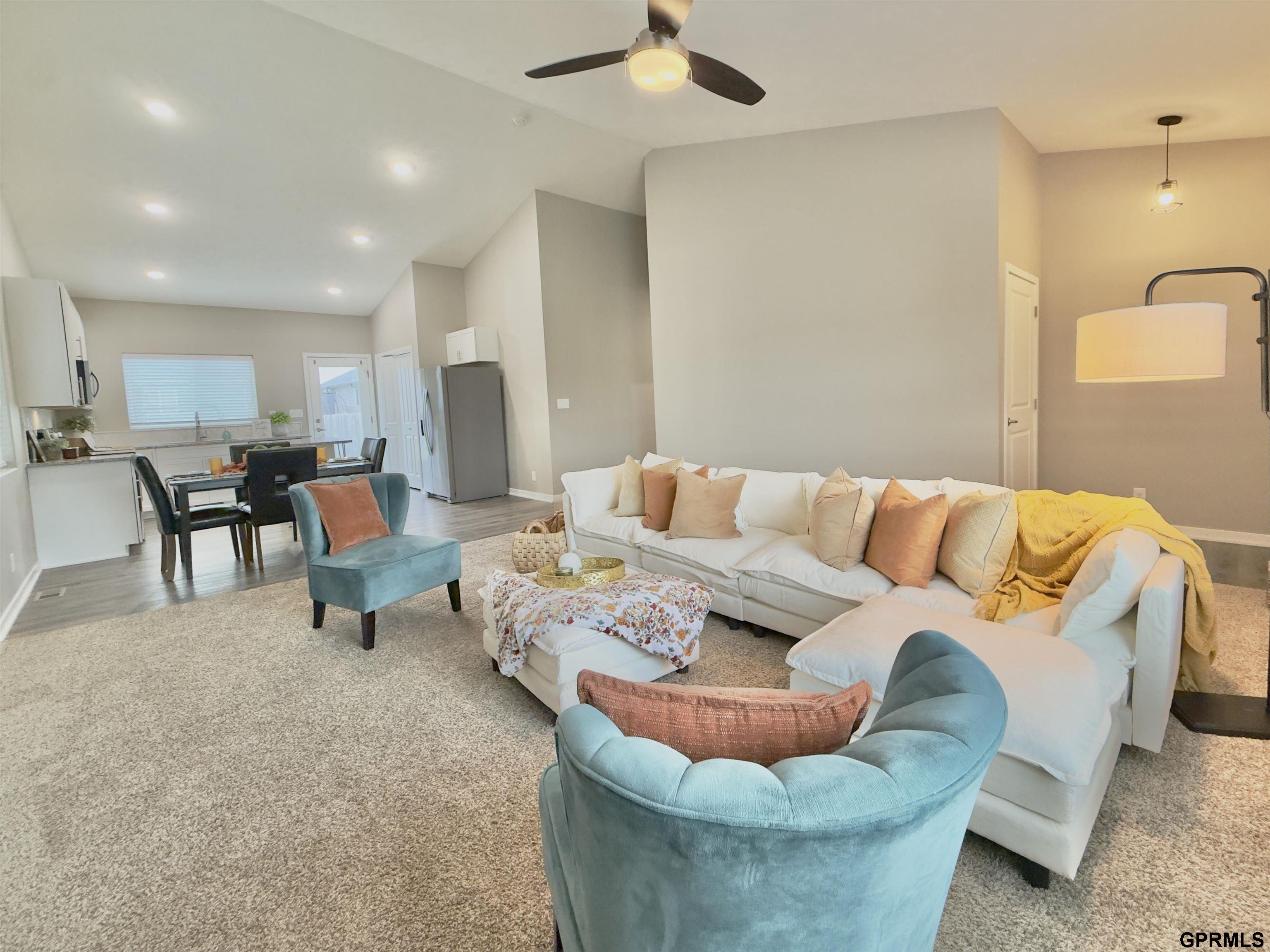 Open-plan living room with a white sectional, teal chairs, and the kitchen and dining area beyond.