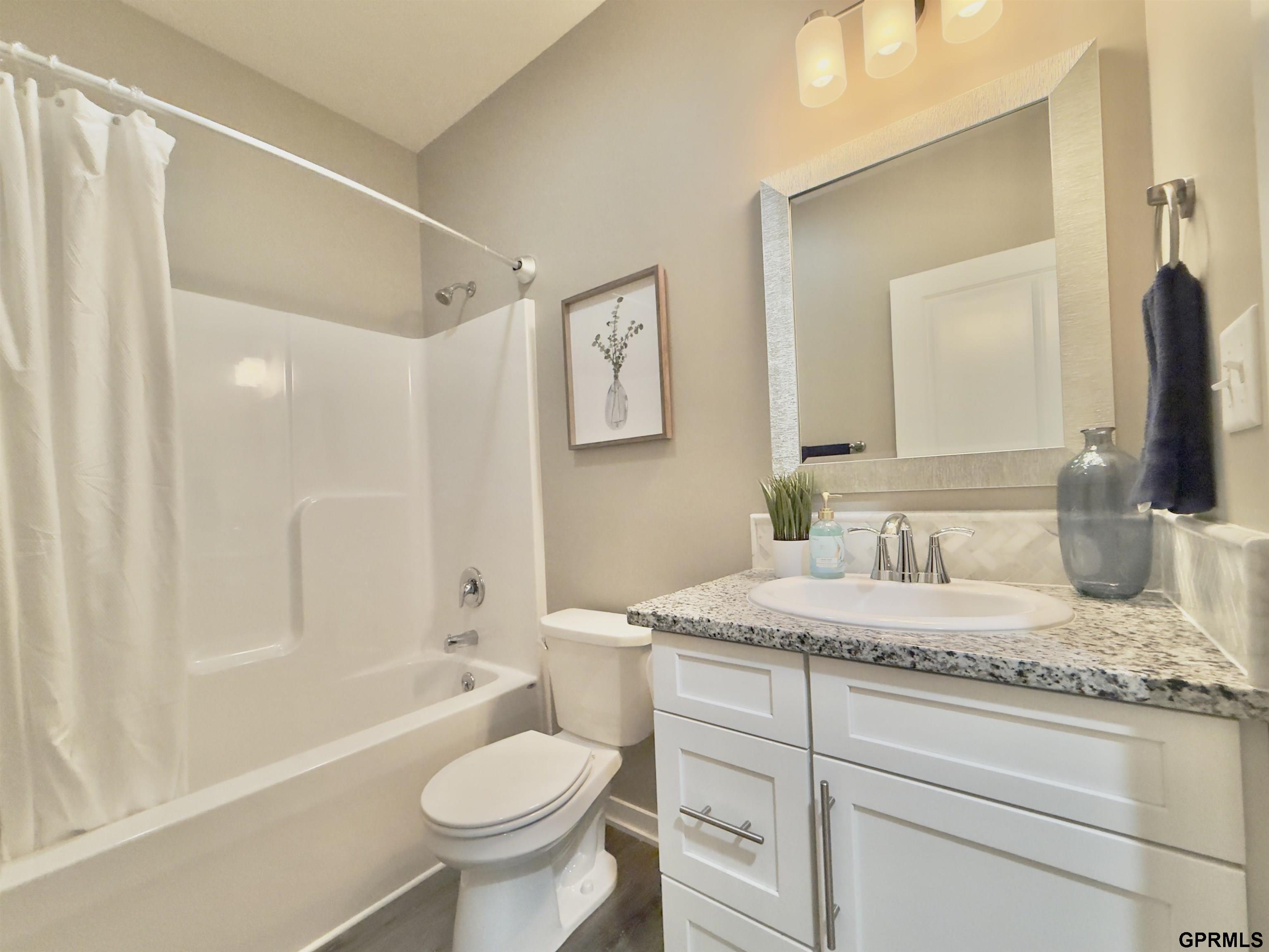 Bathroom with a white tub and shower, toilet, and granite-topped vanity.
