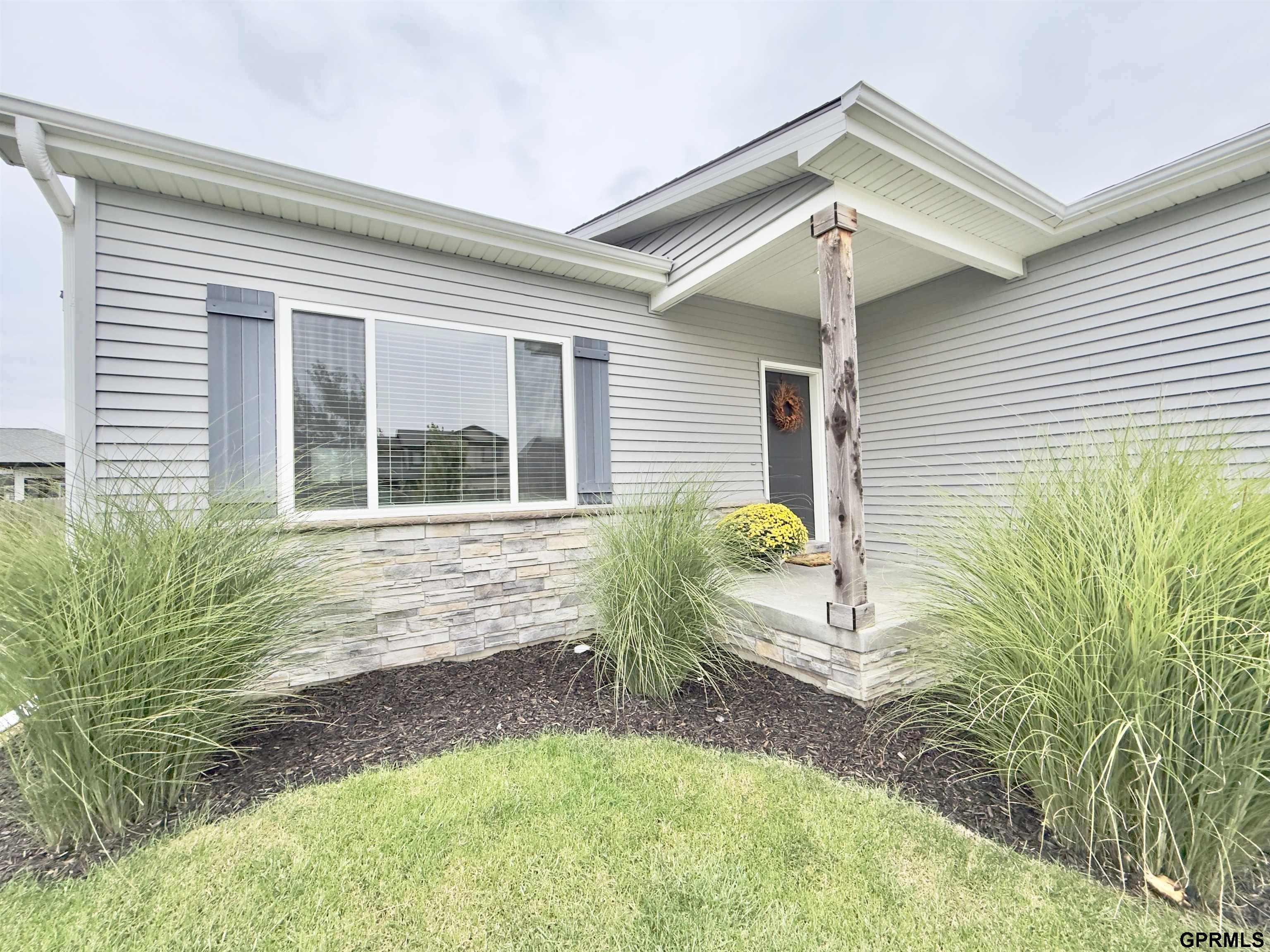 Gray-sided house with a covered entry, stone veneer, and landscaped ornamental grasses.