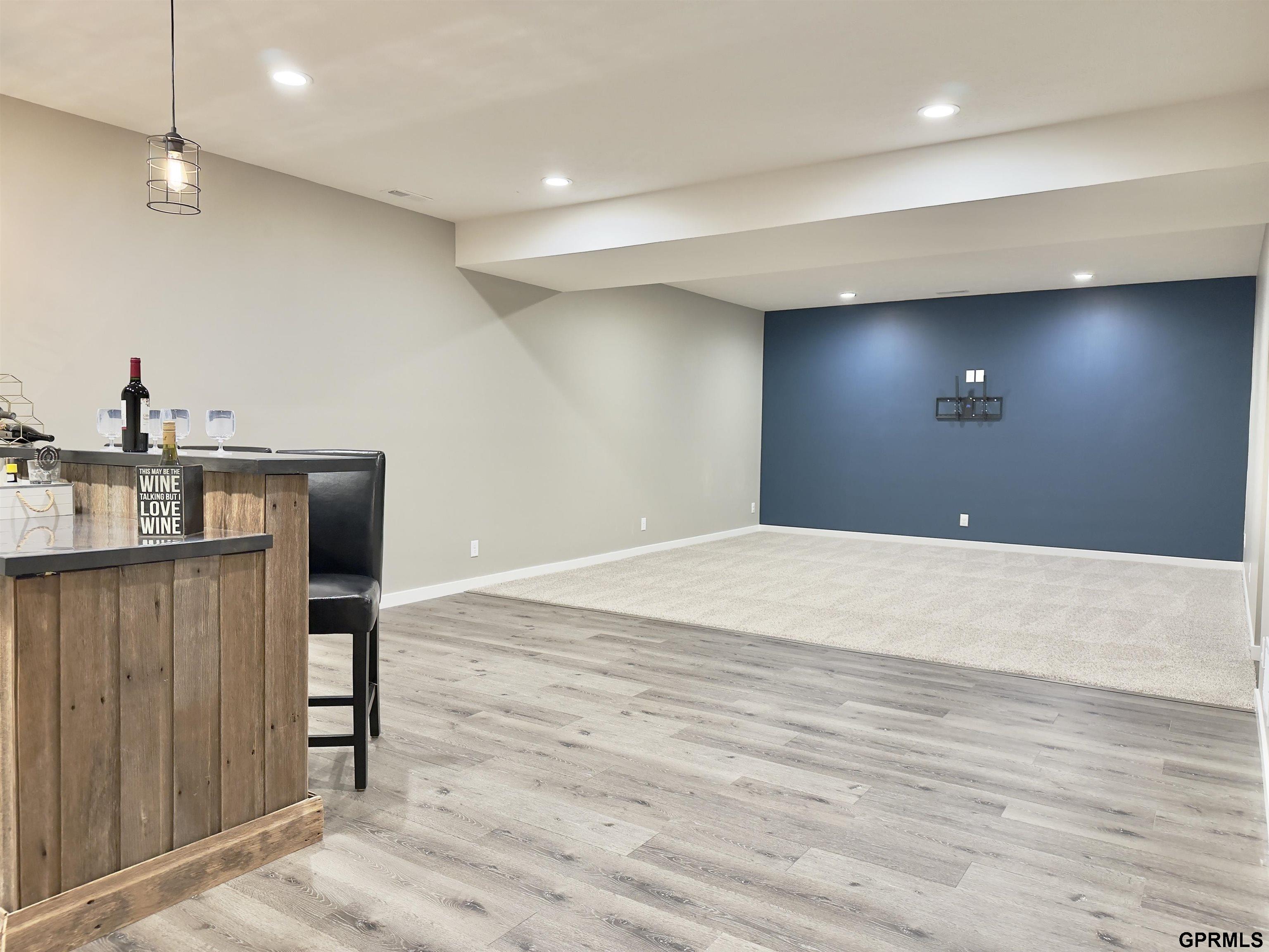 Lower-level recreation room with a wood-front bar, gray flooring, carpeted area, and blue accent wall.