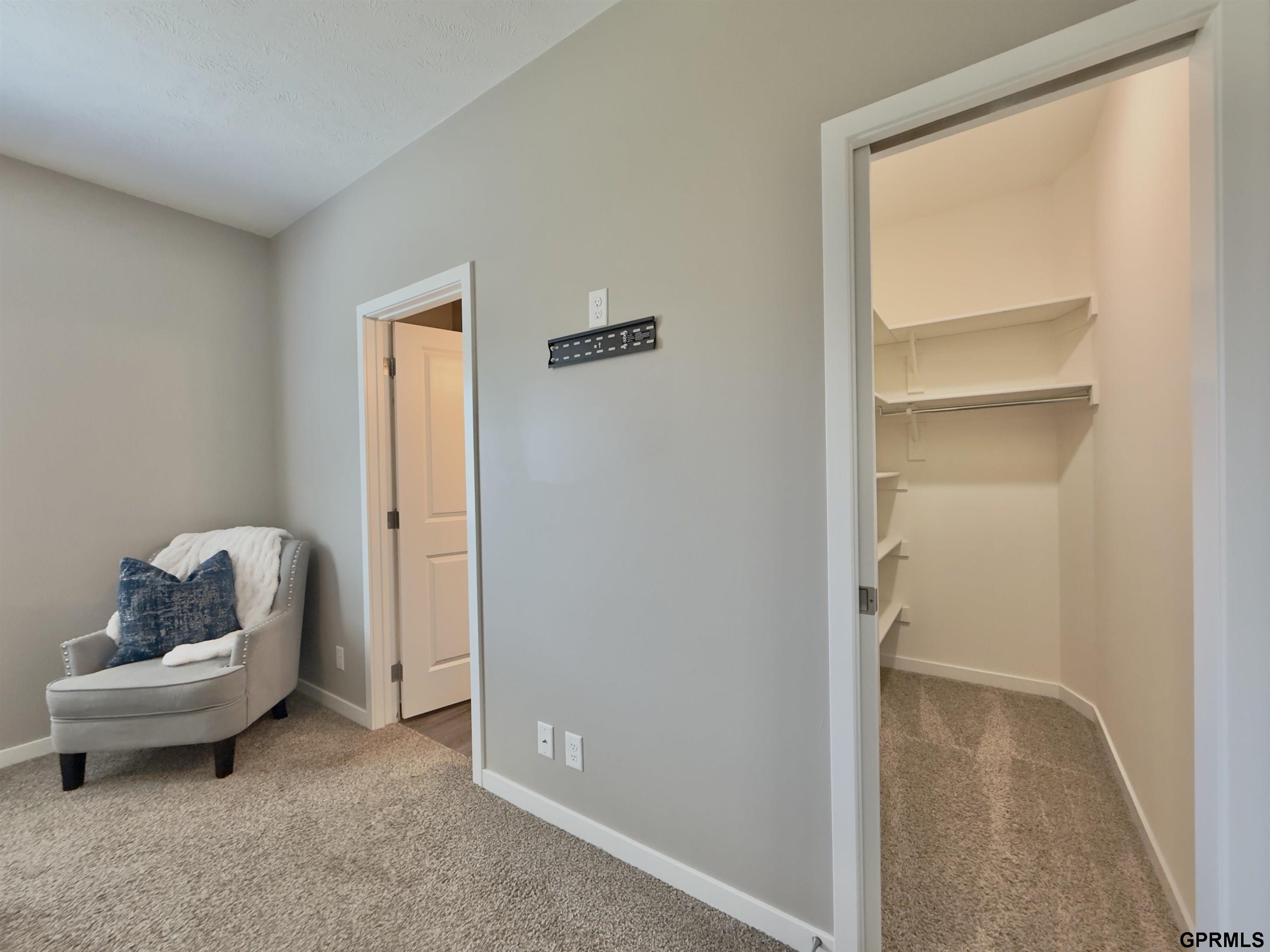 Carpeted bedroom with a gray chair beside an open walk-in closet with built-in shelves.