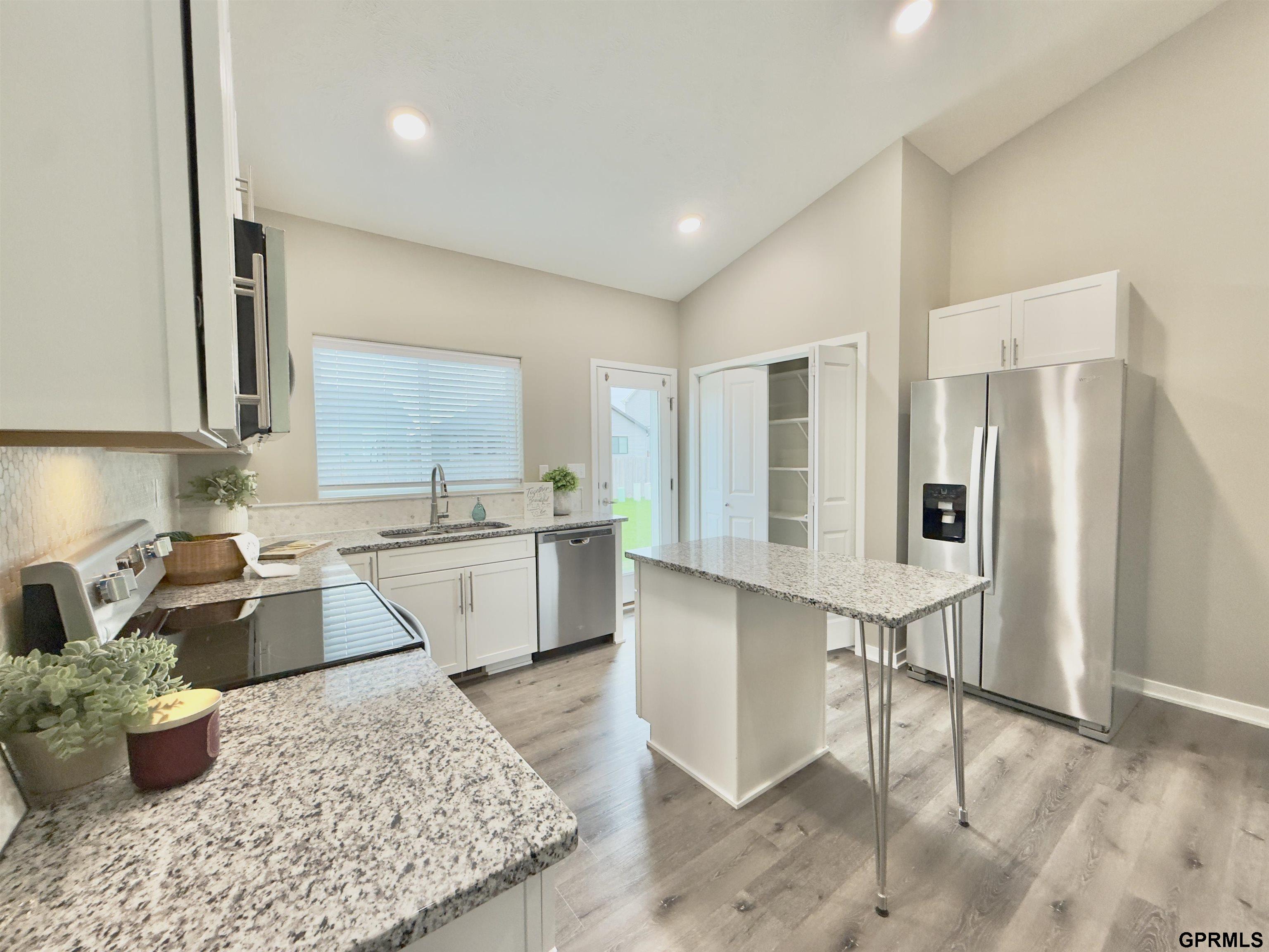 Kitchen with granite counters, a central island, white cabinets, and stainless steel appliances.