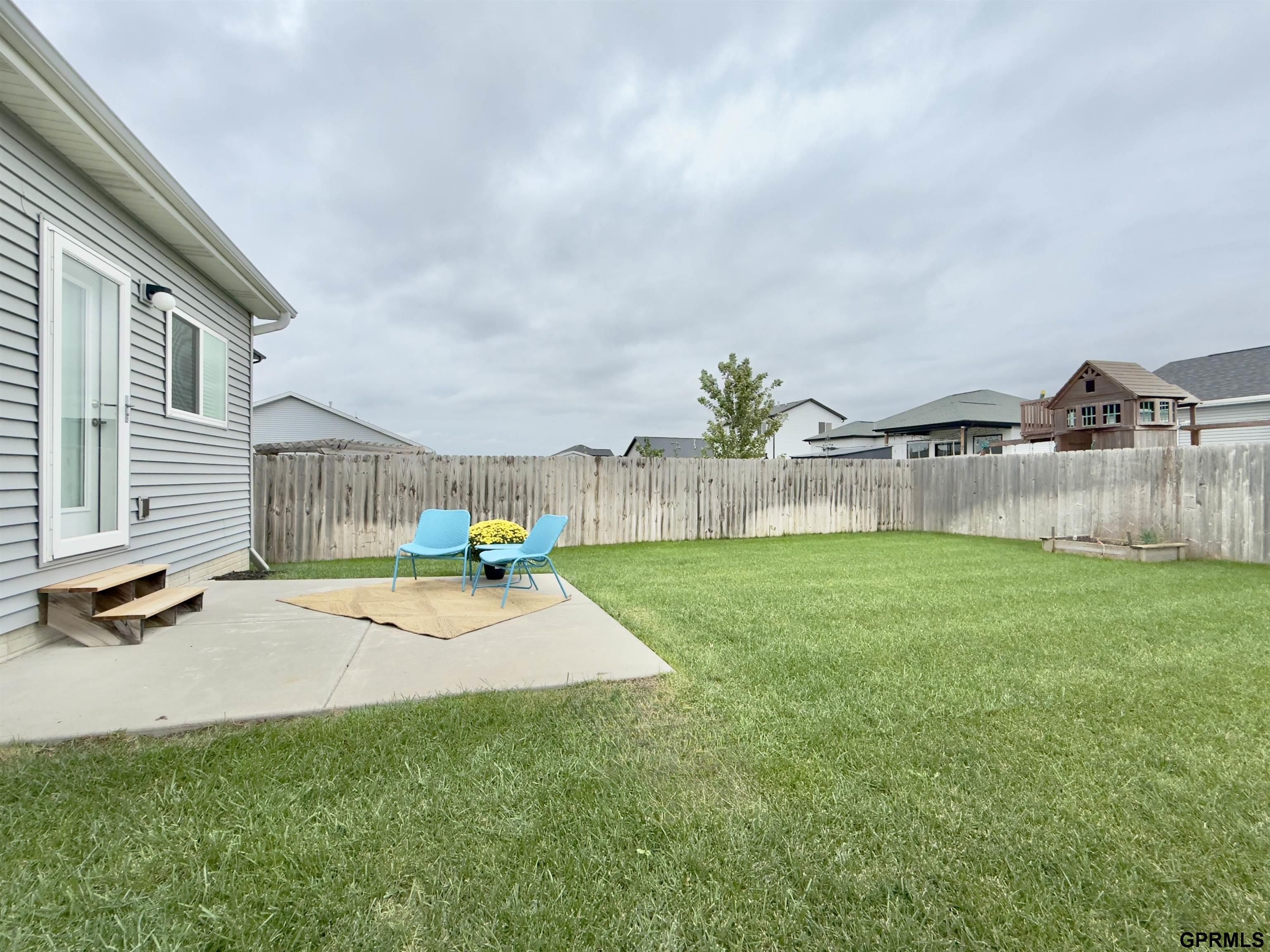 Fenced backyard with a green lawn and patio furnished with turquoise chairs.