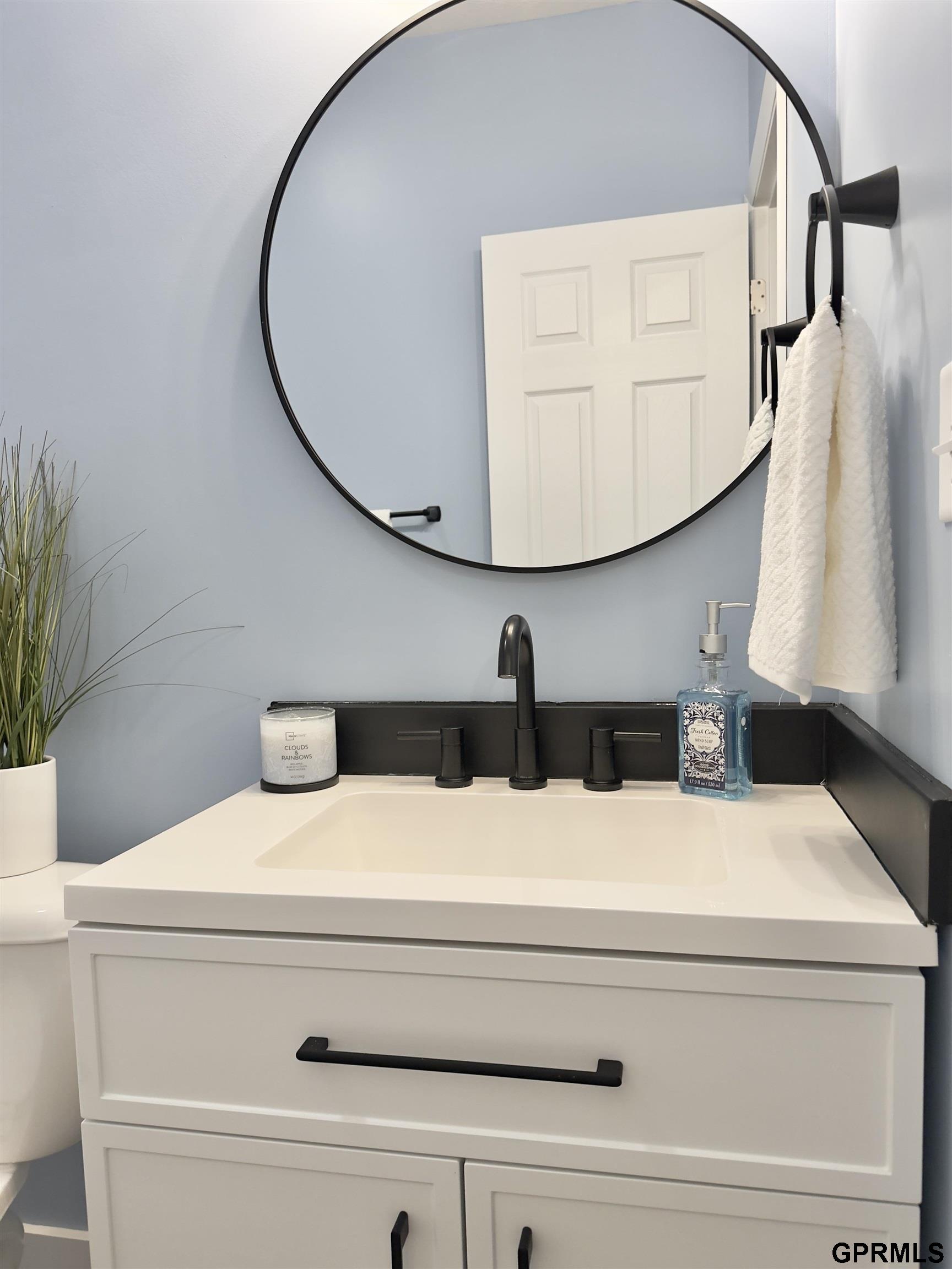 Bathroom vanity with a round black-framed mirror, pale blue walls, and matte black fixtures.