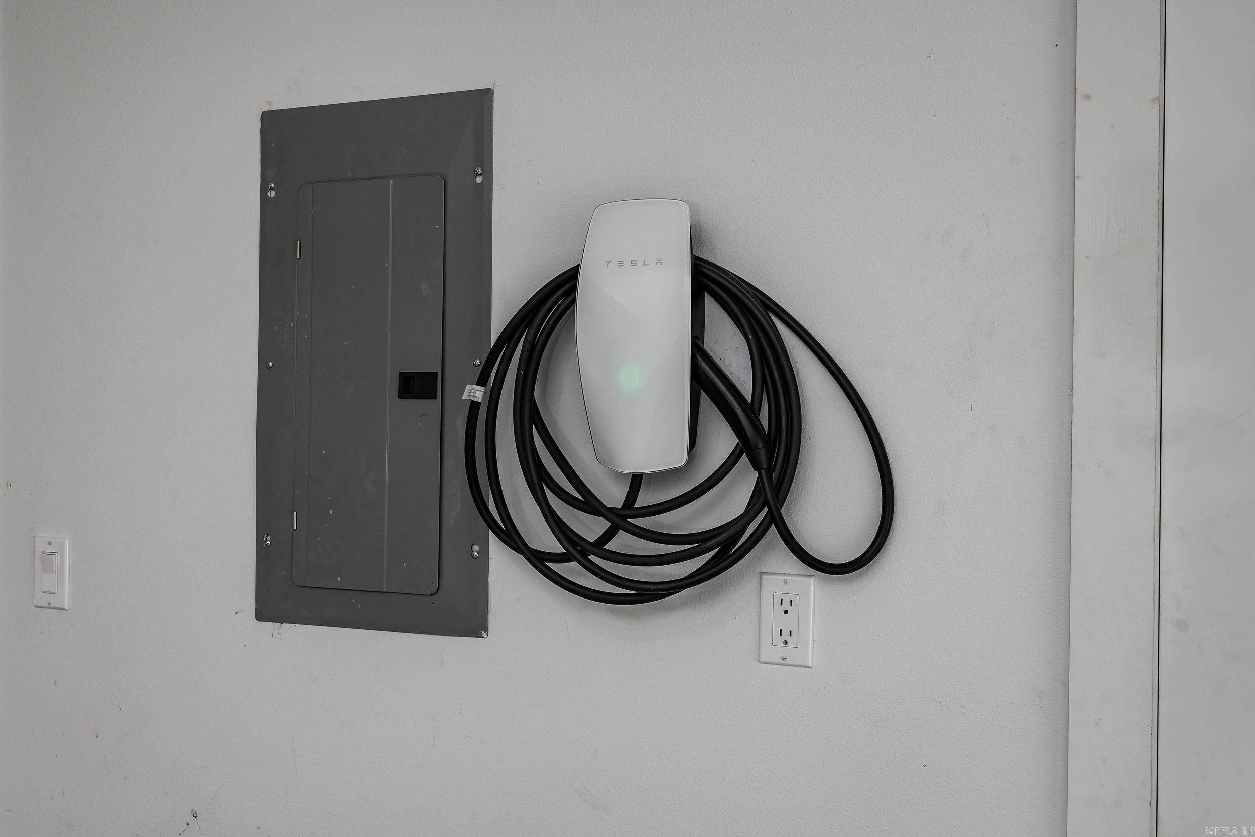 Tesla wall charger with coiled cable mounted beside an electrical panel.