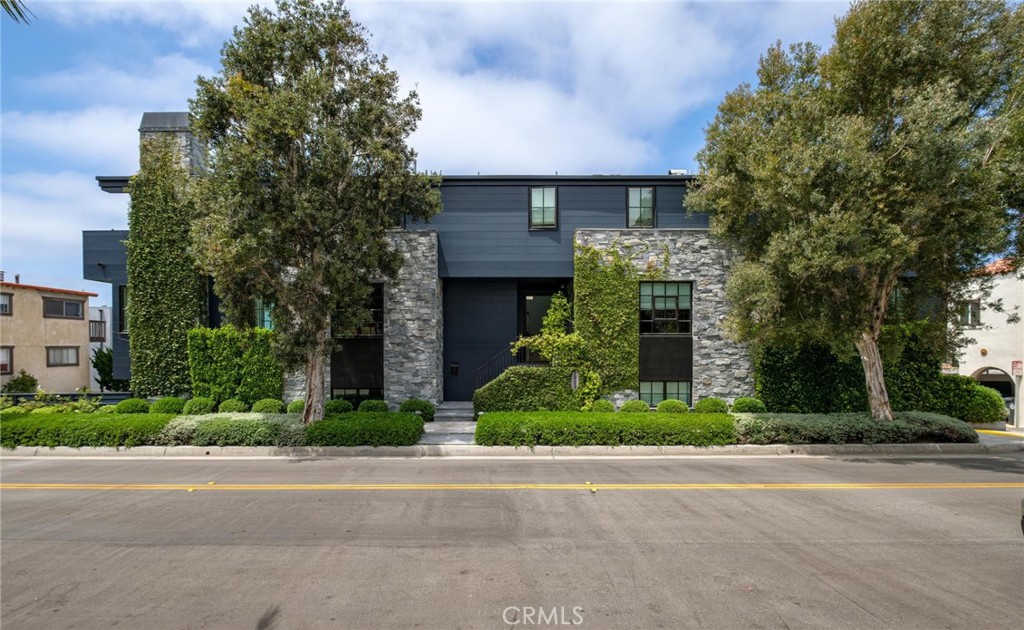 Modern two-story home with dark siding, stone facade, ivy, and mature trees along the street.