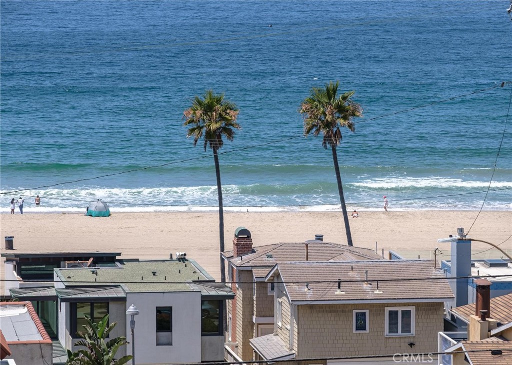 Ocean and sandy beach beyond neighboring rooftops, framed by two palm trees.