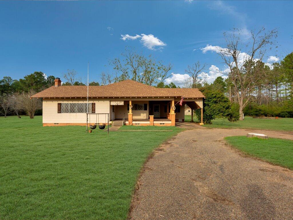 Single-story home with a broad covered porch, brick columns, and a driveway across the lawn.