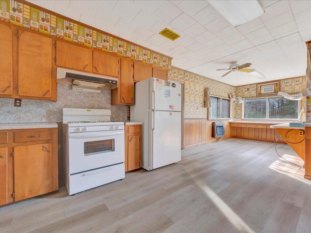 Kitchen with wood cabinets, white appliances, and a window-lined dining area.