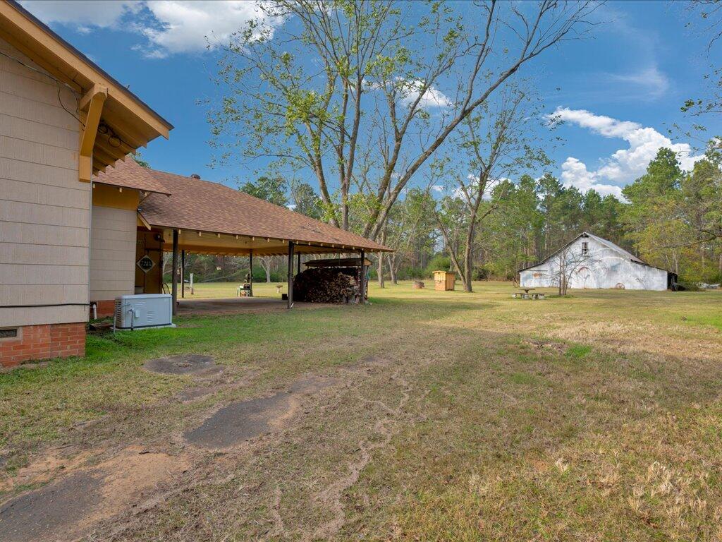 Rural property yard with a firewood-filled carport and a white detached outbuilding.