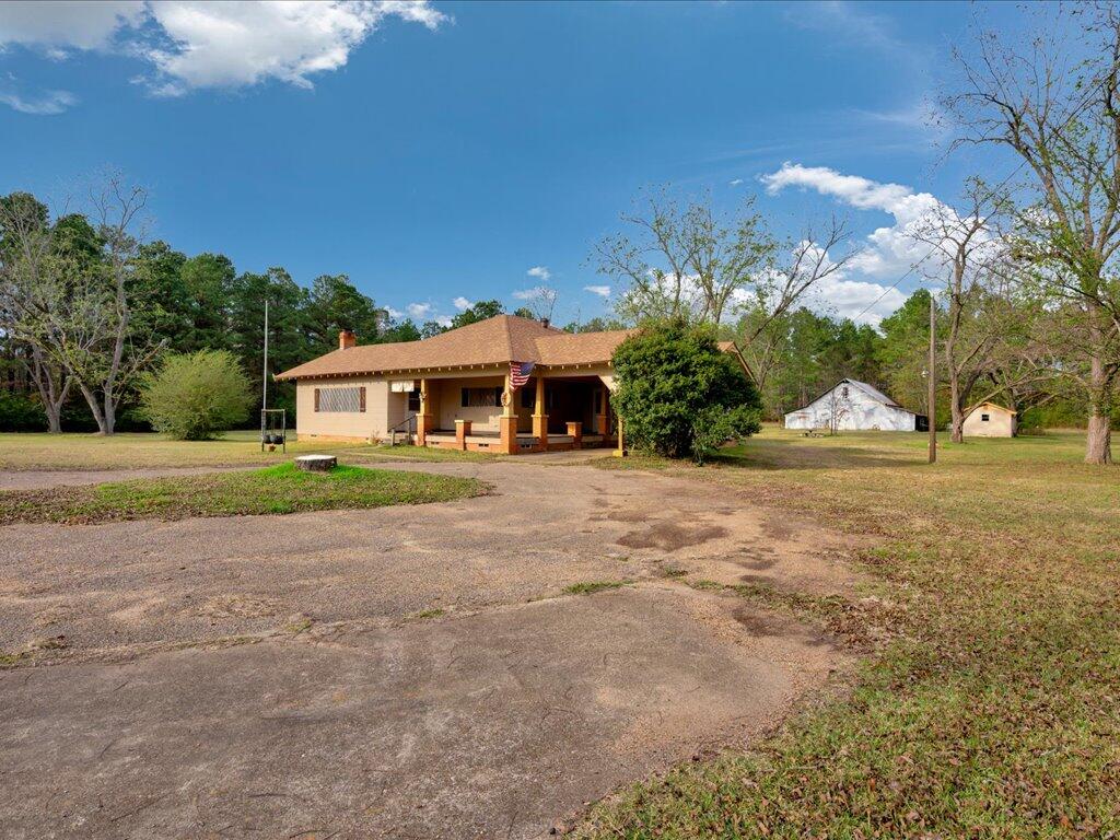 Tan single-story house with a covered porch, broad driveway, and two outbuildings on a rural lot.