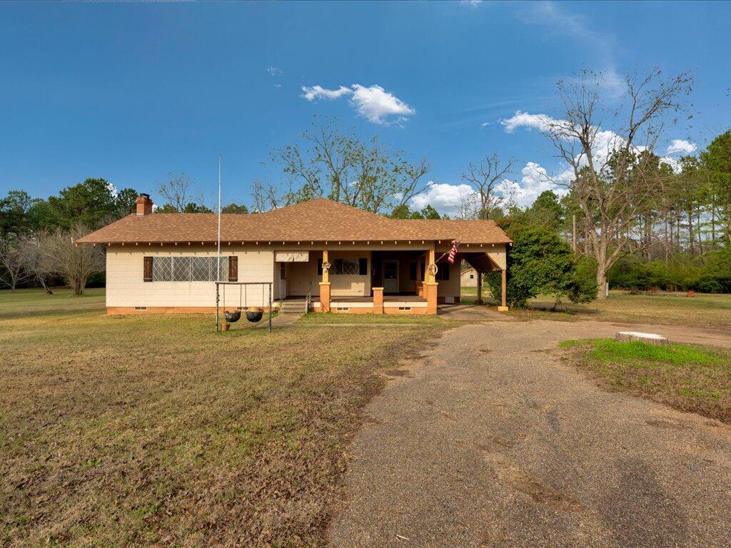 Single-story home with a covered porch, broad lawn, and paved driveway.