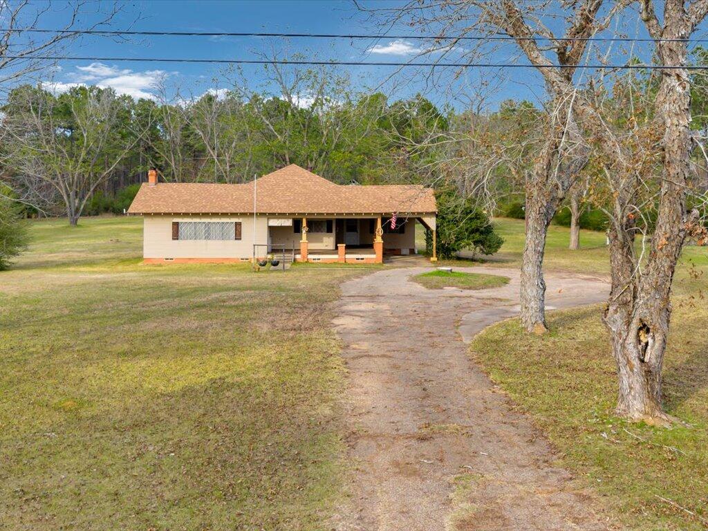 Single-story house with a covered porch set back along a curved driveway among trees.