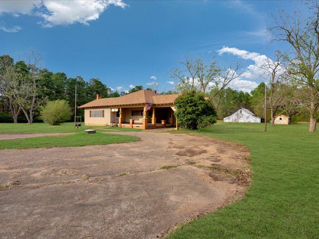 Single-story house with a covered porch, curved driveway, and two outbuildings on a grassy lot.