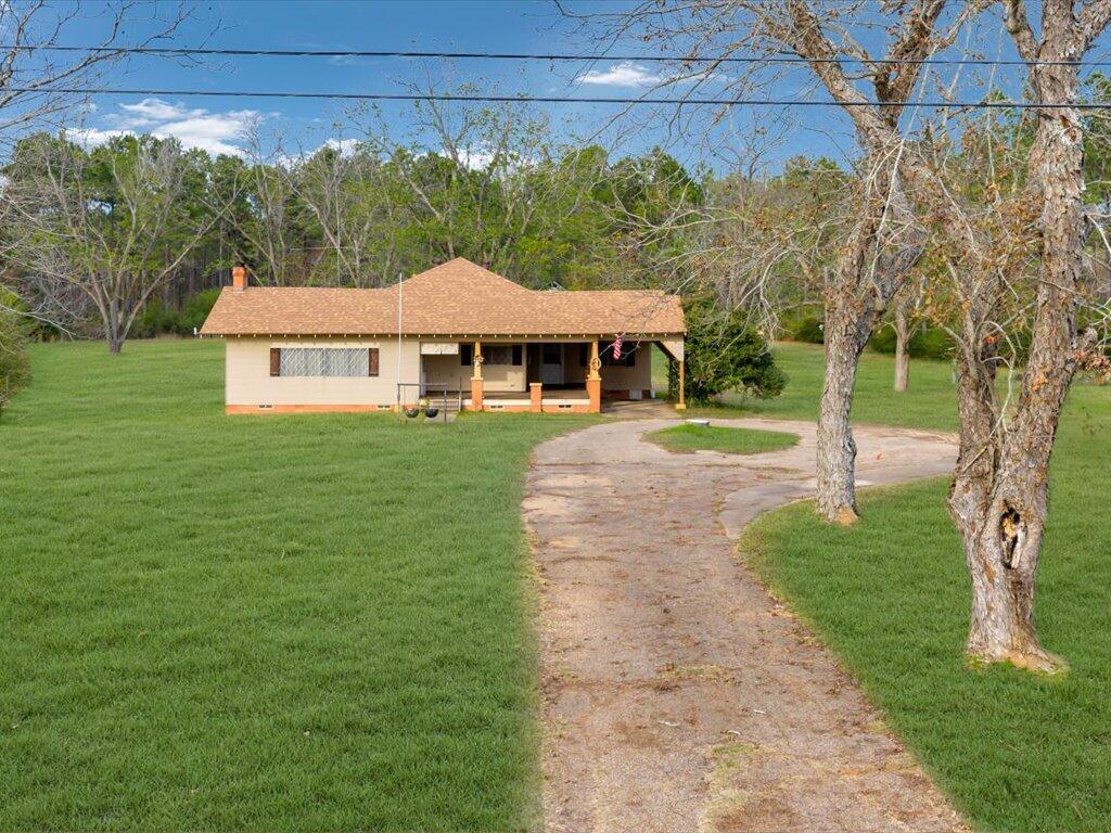 Single-story house with a covered porch, curved driveway, and broad green lawn.
