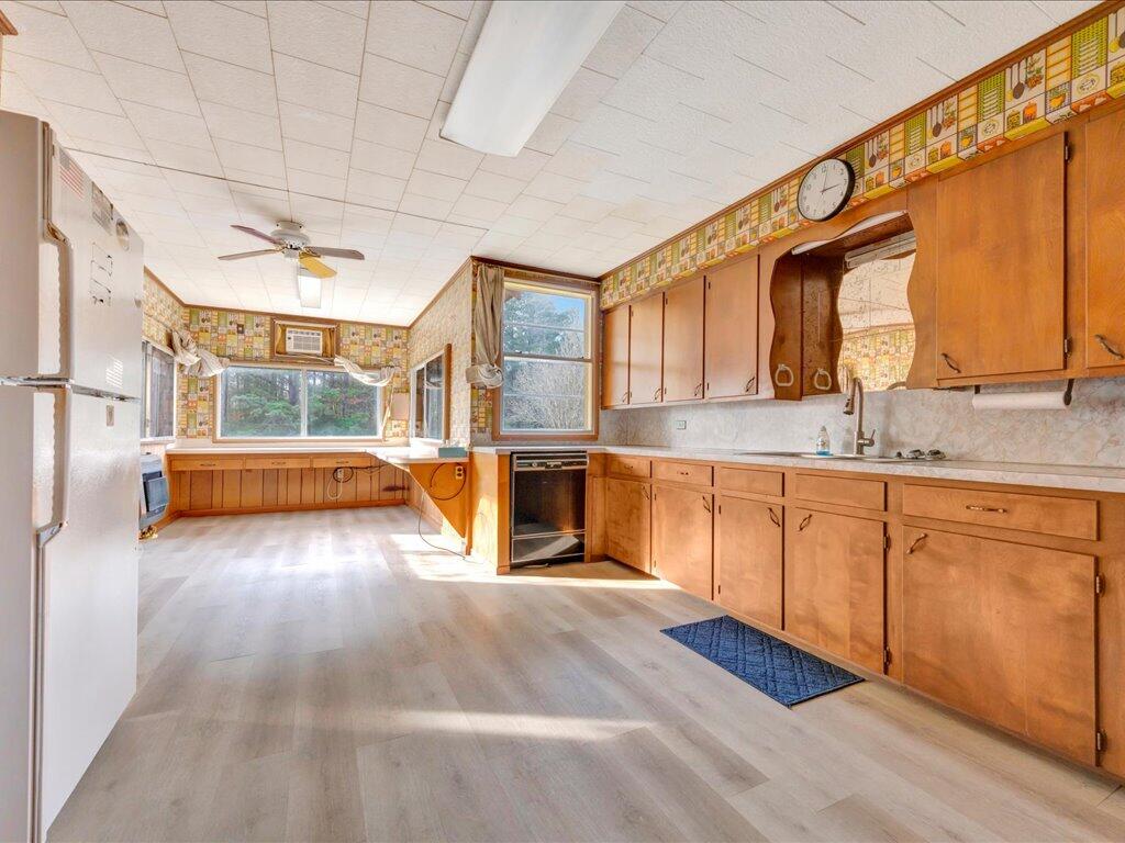 Spacious kitchen with honey-colored cabinets, patterned wallpaper, and large sunlit windows.