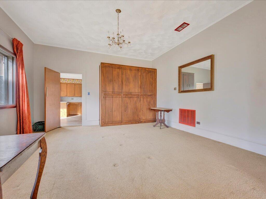Carpeted bedroom with a built-in wooden wardrobe, chandelier, and doorway to the kitchen.