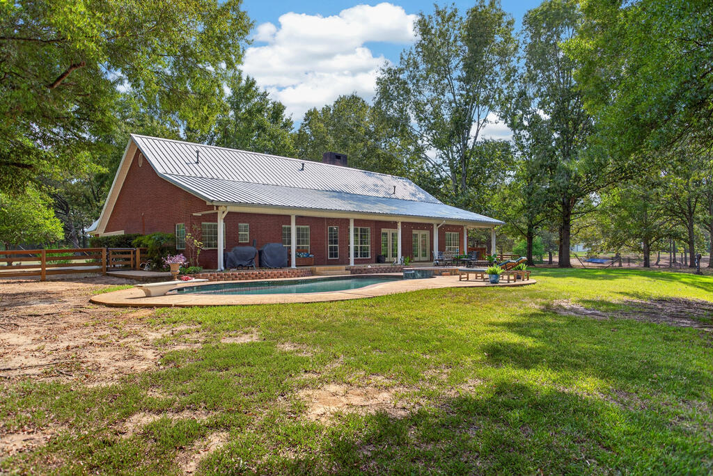 Red-brick home with a metal roof and backyard swimming pool beneath mature trees.