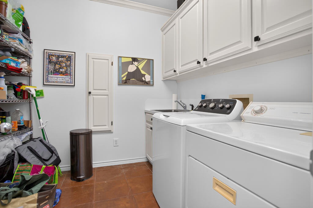 Laundry room with white washer and dryer, upper cabinets, utility sink, and crowded open storage shelves.