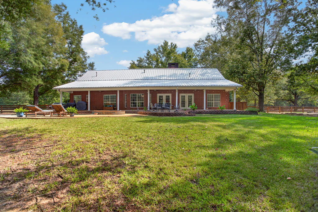 Rear of a red-brick home with a covered patio, outdoor seating, and a broad lawn.