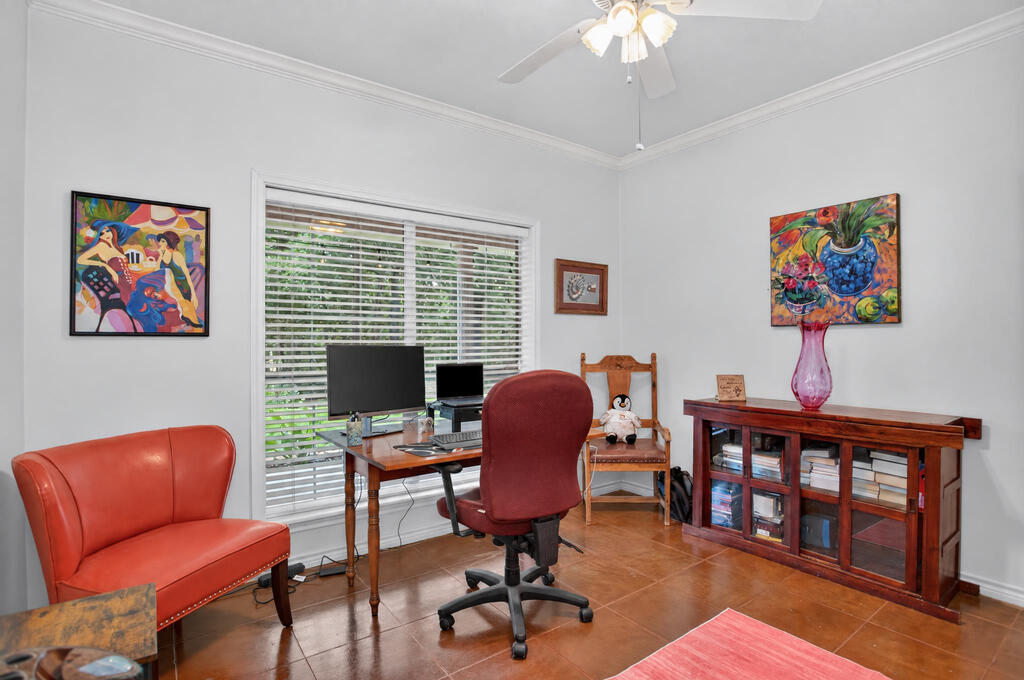 Furnished home office with a computer desk, red leather chair, and colorful artwork.