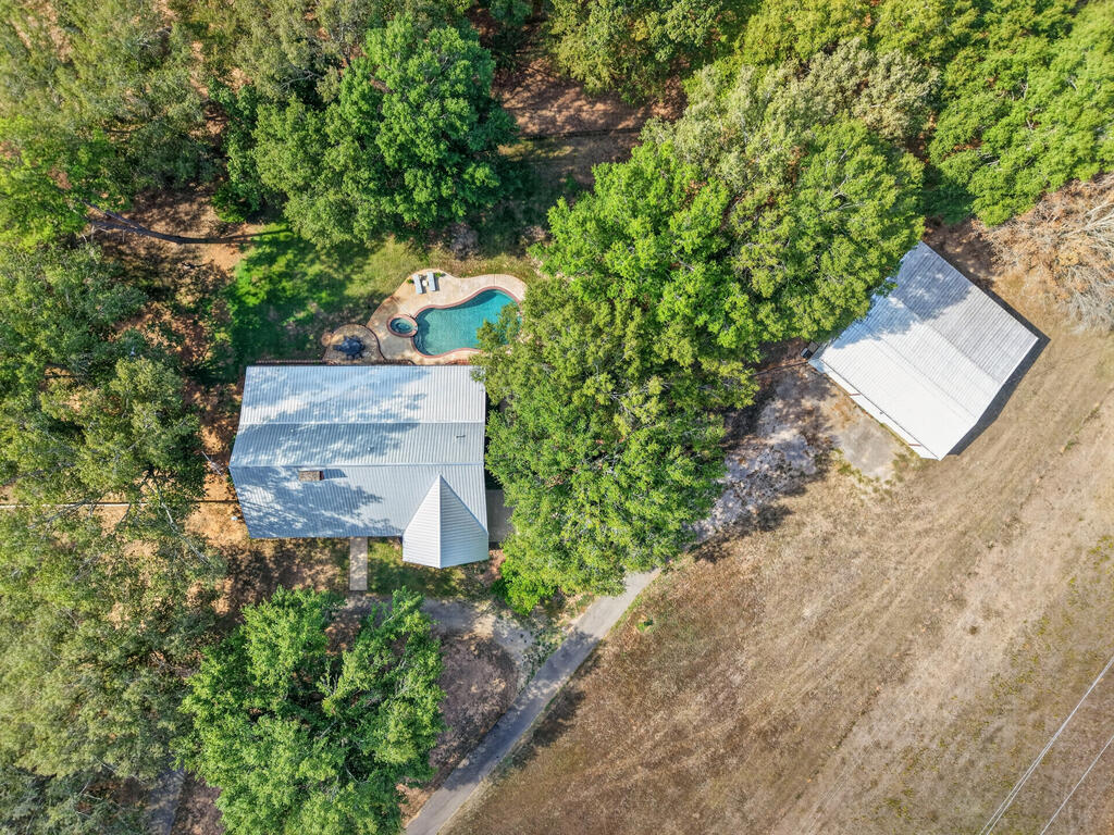 Aerial view of a tree-shaded home, detached outbuilding, and swimming pool.