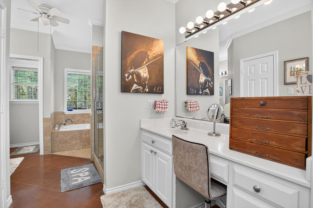 Bathroom with a long white vanity, makeup seat, glass shower, and tiled bathtub.