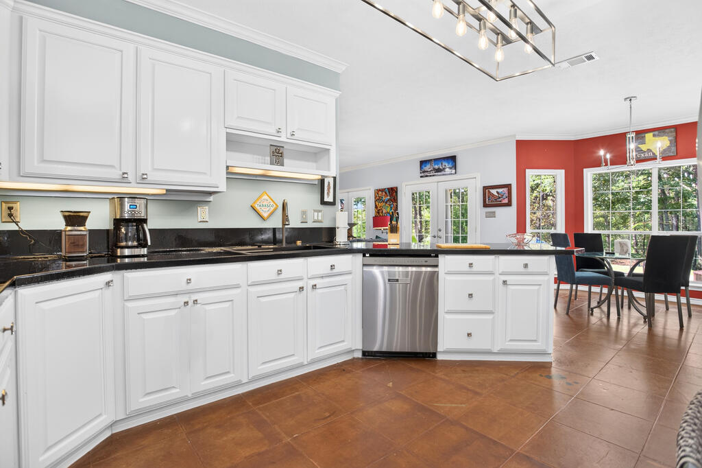 Kitchen with white cabinets, black countertops, stainless steel dishwasher, and adjoining dining area with red walls.