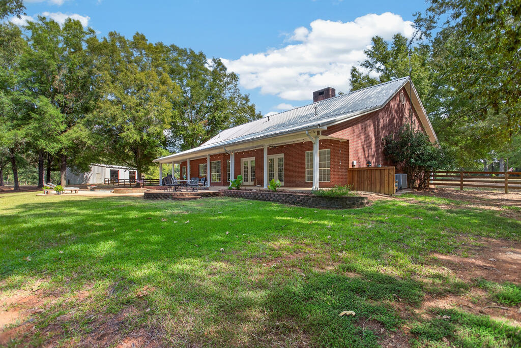 Red-brick home with a covered patio, metal roof, and tree-lined backyard.