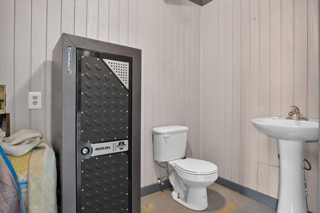 Bathroom with a large gun safe beside a toilet and pedestal sink.