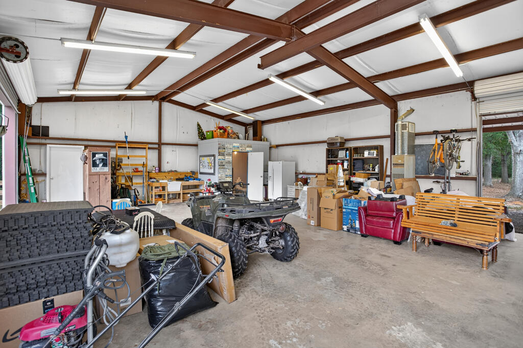 Metal garage with exposed steel beams, utility vehicles, shelving, and stored furniture.