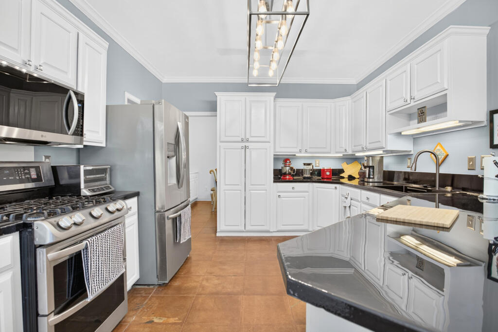 Kitchen with white cabinetry, stainless steel appliances, and a large reflective island.