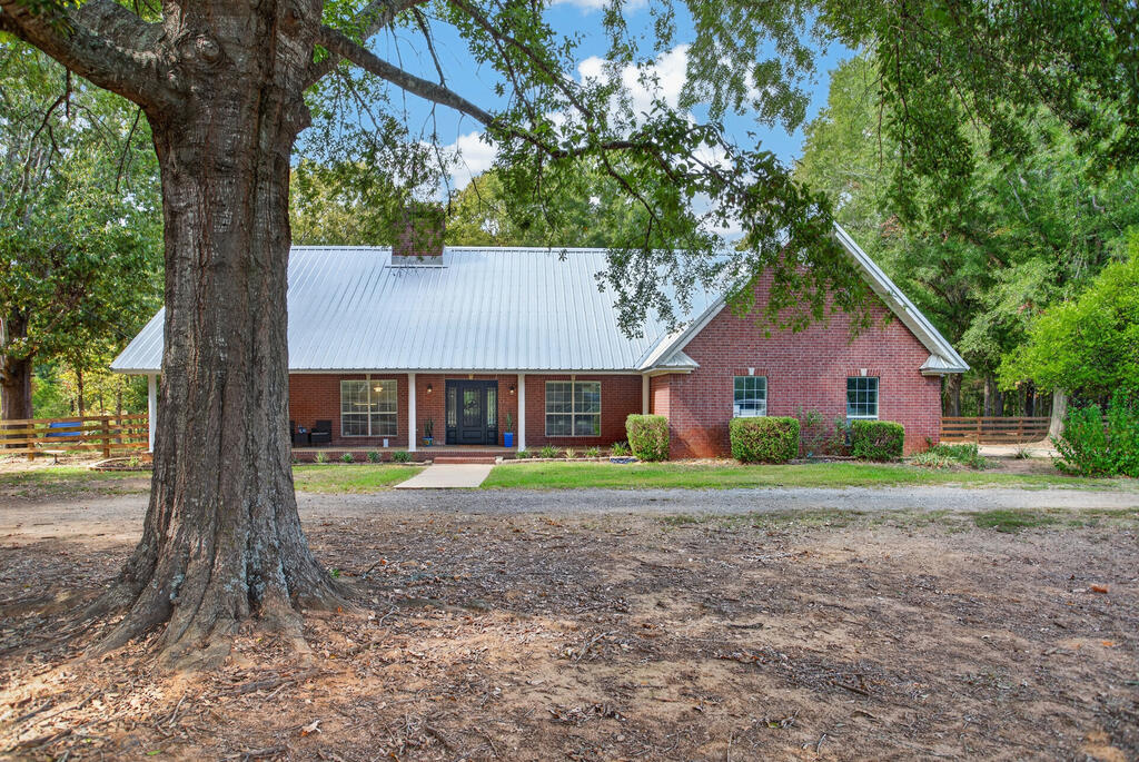 Red brick home with a light metal roof, framed by a large shade tree.