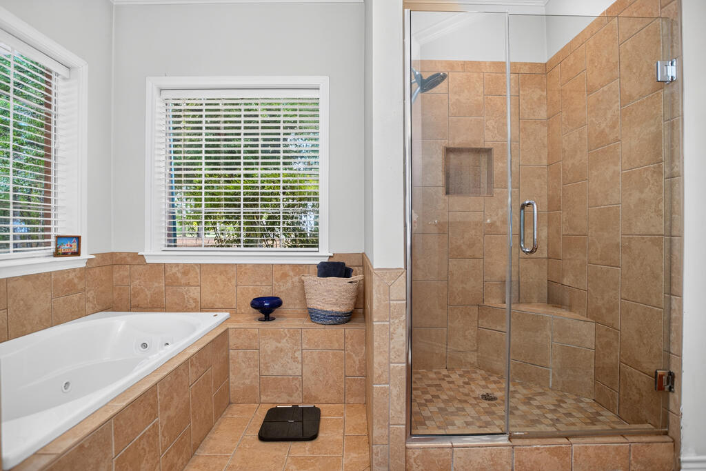 Bathroom with a corner soaking tub and glass-enclosed tan-tiled walk-in shower.