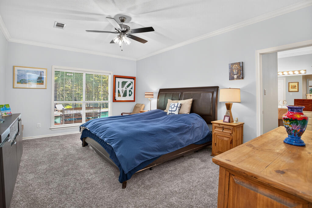Furnished bedroom with a blue-covered bed, gray carpet, and wide windows with blinds.