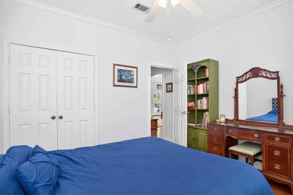 Bedroom with a blue-covered bed, green bookcase, and wooden vanity with an ornate mirror.