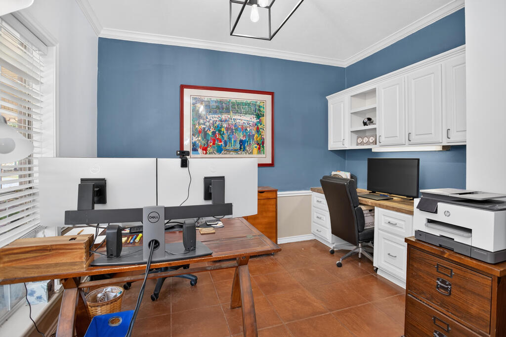 Home office with blue walls, white built-in cabinets, multiple monitors, and a wooden desk.