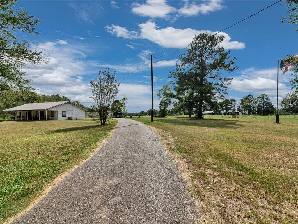 Rural property with a paved driveway, white building, open lawn, mature trees, and an American flag.
