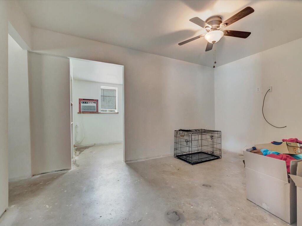 Unfinished interior room with a concrete floor, ceiling fan, and wire pet crate.
